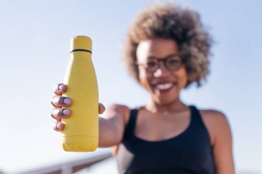 Sarı su şişesi tutan bir koşucunun elinde seçici bir odak ile fotoğraf, spor ve aktif yaşam tarzında susuzluk kavramı, metin için kopyalama alanı