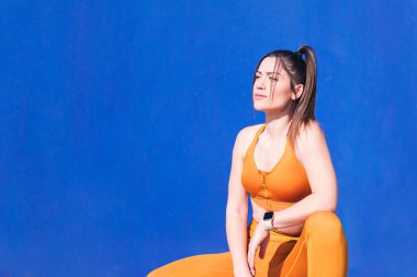 Beyaz tenli sporcu kadın mavi arka planda poz verirken çömeliyor, spor ve sağlıklı yaşam tarzı kavramı, metin için kopya alanı