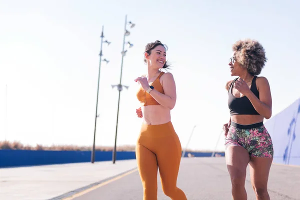 two animated female friends smiling happy running in a athletic track in a sunny day, concept of friendship and active lifestyle, copy space for text