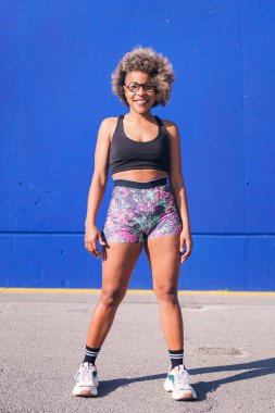 Gülümseyen Afro-Amerikan sporcu kadın mavi arka planda kameraya bakıyor, spor anlayışı ve aktif yaşam tarzı
