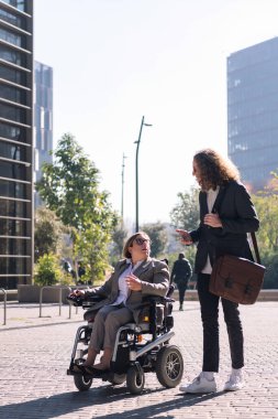 İş adamı ve kadın tekerlekli sandalyede finans bölgesinde ofis binaları arasında yürürken konuşuyor, çeşitlilik kavramı ve şehir yaşam tarzı, metin için kopya alanı