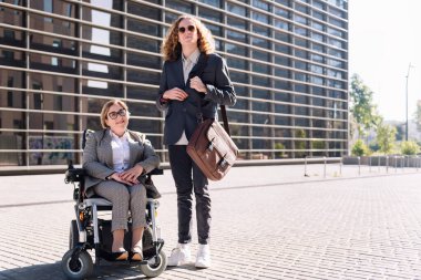 Tekerlekli sandalyedeki iş adamı ve kadın finans bölgesindeki ofis binasının önündeki kameraya bakıyor, çeşitlilik kavramı ve şehir yaşam tarzı