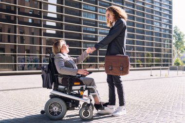 İş adamı ve kadın, finans bölgesinde ofis binasının önünde el sıkışırken tekerlekli sandalyede gülümserken, çeşitlilik kavramı ve şehir yaşam tarzı, metin için kopya alanı