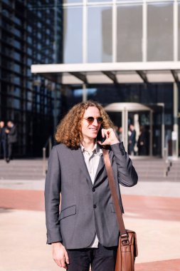 Finans bölgesinde cep telefonuyla konuşan gülümseyen genç iş adamı, iletişim ve kentsel yaşam tarzı kavramı, metin için kopyalama alanı