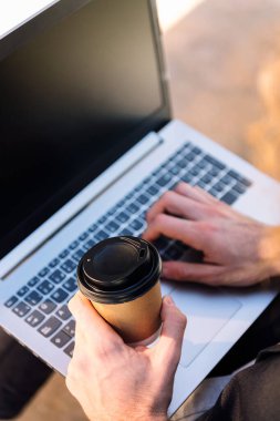 Bilgisayarla çalışırken kahve içen tanınmamış bir adamın üst görünümü, iş ve teknoloji kavramı, kahve üzerine seçici odaklanma, metin için metin alanı