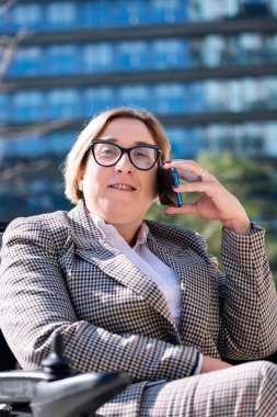 Tekerlekli sandalye kullanan gülümseyen iş kadını finans bölgesinde cep telefonuyla konuşuyor, iletişim teknolojisi ve kentsel yaşam tarzı kavramı, metin için kopyalama alanı