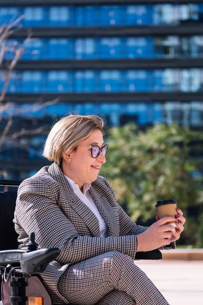 smiling businesswoman using wheelchair with a coffee at hand outdoors at the financial district, concept of diversity and urban lifestyle, copy space for text