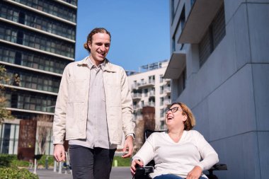 Bir çift genç adam ve kadın elektrikli sandalye kullanarak sohbet ederken mutlu bir şekilde gülüyorlar, arkadaşlık ve çeşitlilik kavramı.