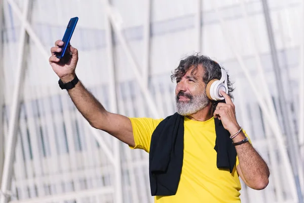 senior sports man listening to music with headphones while taking a selfie photo with his mobile phone, concept of active lifestyle in middle age