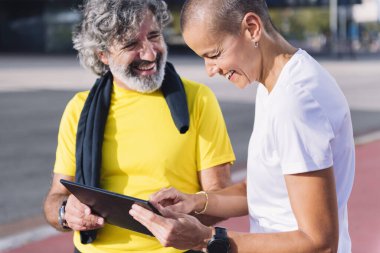 Son sınıf sporcusu orta yaşlarda sağlıklı ve aktif yaşam biçimi kavramı olan tablet üzerinde çalışırken kişisel antrenörle gülerken mutlu oluyor.