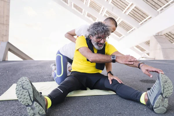 senior sports man stretching legs with help of his personal trainer, concept of active and healthy lifestyle in middle age