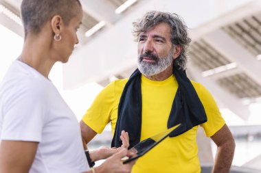 Son sınıf sporcusu antrenmanını tabletle izliyor ve sonuçları kişisel antrenörüyle tartışıyor. Sağlıklı ve aktif yaşam tarzı kavramı.