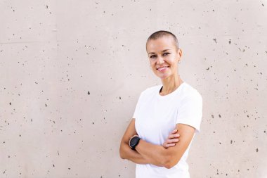 Kısa saçlı, gülümseyen, kolları çaprazlanmış, kameraya bakan genç bir kadın.