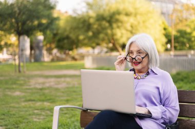 Gözlüklü, bilgisayar kullanan, parktaki bankta oturan, teknoloji ve yaşlı insanların boş vakitleri olan, metin için kopyalama alanı olan güzel bir son sınıf kadını.