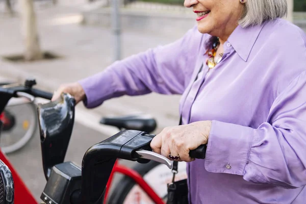 unrecognizable senior woman taking rental bike from parking row, concept of sustainable mobility and active lifestyle in elderly people