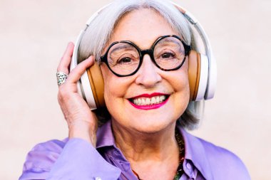 Kameraya bakan, kulaklıkla müzik dinlemekten keyif alan, yaşlı insanların boş vakitleri ve aktif bir yaşam tarzı olan gülümseyen yaşlı bir kadının portresini yakından çek.