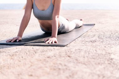 Spor kıyafetleri içinde tanınmayan bir kadın deniz kenarında yoga yapıyor, zihinsel rahatlama ve sağlıklı yaşam tarzı kavramı, metin için kopyalama alanı