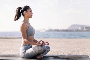 Spor kıyafetli genç Asyalı kadın yoga minderi üzerinde meditasyon yapıyor, zihinsel rahatlama ve sağlıklı yaşam tarzı kavramı, metin için kopya alanı