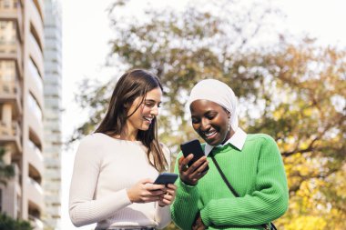 İki genç kadın mutlu gülümsüyor cep telefonlarına bakıyorlar, arkadaşlık ve teknoloji kavramı, metin için kopyalama alanı