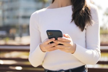 Cep telefonunu açık havada kullanan tanınmayan beyaz kadın, iletişim teknolojisi ve modern yaşam tarzı kavramı.