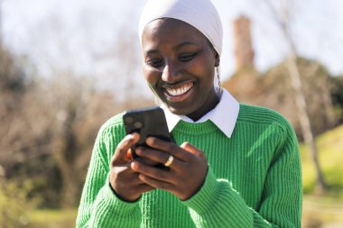 Genç Afrikalı kadın açık havada cep telefonu kullanmaktan mutlu, iletişim teknolojisi ve modern yaşam tarzı kavramı