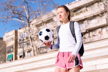 Beyaz kadın elinde bir futbol topuyla şehirde yürüyor, spor anlayışı ve aktif yaşam tarzı, metin için kopyalama alanı