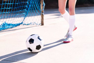 Bir futbol oyuncusunun ayaklarına yakın durarak bir futbol topuna doğru yürürken bir şehir sahasının, spor konseptinin ve aktif yaşam tarzının yanında.