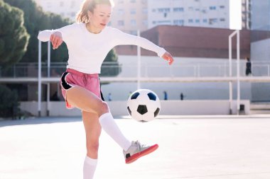 Kadın futbolcu şehir futbol sahasında ayaklarıyla topa vuruyor, spor anlayışı ve aktif yaşam tarzı.