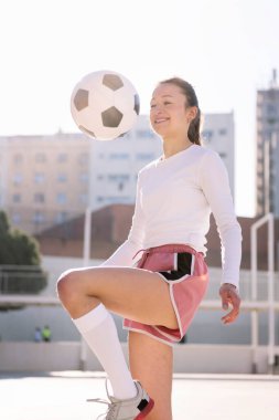 Gülümseyen bayan futbolcu şehir futbol sahasında diziyle topa vuruyor, spor ve aktif yaşam tarzı kavramı