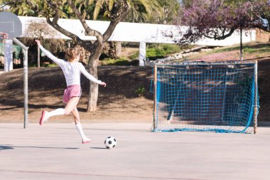 Şehir sahasında, spor anlayışı ve futbol yaşam tarzında futbol topuna tekme atan tanınmayan beyaz bir kadının arka penceresi.
