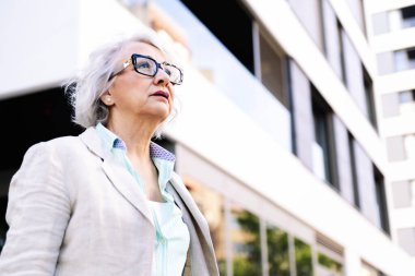 Bir binanın yanında yürüyen şık, olgun bir kadının portresi, yetişkinlikte kentsel yaşam konsepti, metin için kopyalanma alanı