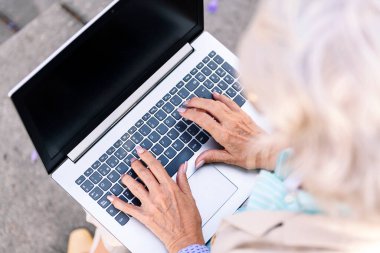 Yetişkinlik çağında, olgun bir kadının ellerinin kentte oturup dizüstü bilgisayarda, teknoloji ve modern yaşam tarzında yazı yazması.
