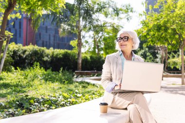 Şehir parkında dizüstü bilgisayar kullanarak mutlu gülümseyen orta yaşlı bir kadın teknoloji kavramı ve modern olgun insan yaşam tarzı, metin için metin alanı