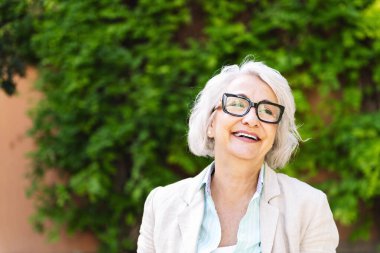 Orta yaşlı bir kadının portresi bulanık yeşil bitkilerle mutlu gülüyor, olgun insan yaşam tarzı konsepti, metin için metin alanı