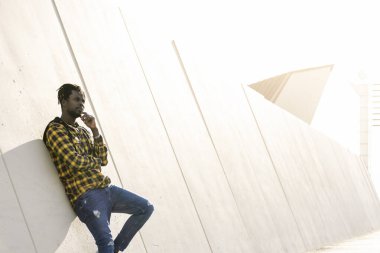 Genç siyah adam günbatımında modern beton bir yapıya yaslanıyor, yaşam tarzı konsepti.