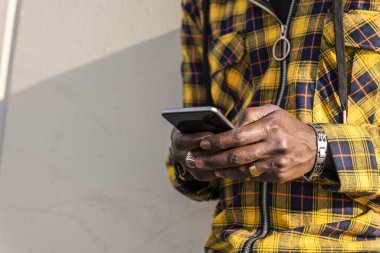 Tanımlanamayan Afrikalı genç bir adamın elleri telefonuna mesaj yazıyor modern beton bir yapıya yaslanıyor, yaşam tarzı ve teknoloji kavramına.