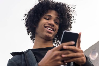 Gülümseyen Afrikalı Amerikalı hippi erkek kıvırcık saçlı şehirde cep telefonu kullanıyor, iletişim teknolojisi ve şehir yaşam tarzı kavramı