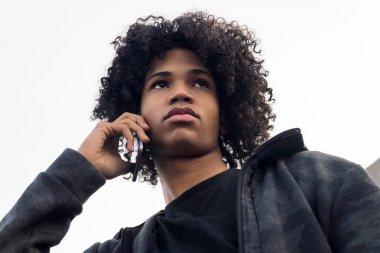 Ciddi Afro-Amerikan erkek kıvırcık saçlı, sokakta telefon görüşmesi yaparken başka tarafa bakıyor.