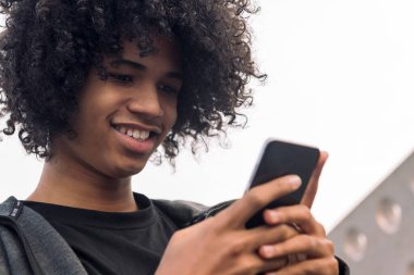 Gülümseyen Afrikalı Amerikalı hippi erkek kıvırcık saçlı cep telefonu, iletişim teknolojisi ve şehir yaşam tarzı kavramı kullanıyor.