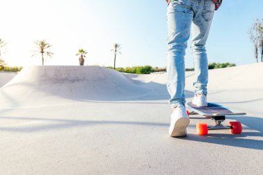 Güneşli bir yaz gününde kaykay parkında kot pantolon ve spor ayakkabılarla tanınmaz hale gelmiş bir patenci.