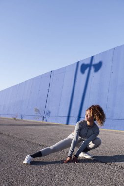 Spor giyim sektöründe yetişkin bir bayan sporcu asfalt yolda, şehir sporu ve sağlıklı yaşam tarzı kavramında yan çömelme performansı sergiliyor.