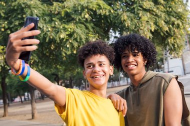 Çok ırklı iki ergen gülümseyerek cep telefonu, gençlik yaşam tarzı ve iletişim teknolojisi ile selfie çekiyorlar.