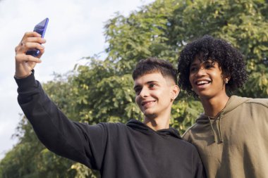 Çok ırklı iki ergen gülümseyerek cep telefonu, gençlik yaşam tarzı ve iletişim teknolojisi ile selfie çekiyorlar.