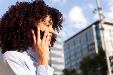 Şehirdeki akıllı telefondan konuşan kıvırcık saçlı bir kadın girişimcinin portresi.