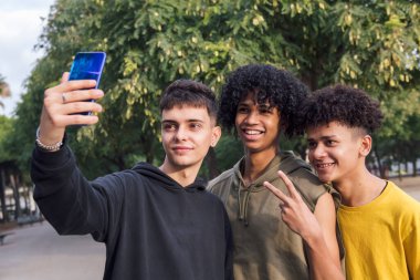 Çok ırklı üç ergen gülümseyerek cep telefonu, gençlik yaşam tarzı ve iletişim teknolojisi ile selfie çekmekten mutlu oluyorlar.