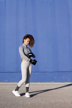 Kararlı kadın boksör mavi arka plan, güç ve sağlıklı yaşam konsepti üzerinde çalışırken boks eldiveni takıyor, metin için kopya alanı