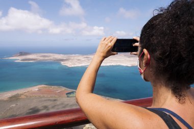 Graciosa Adası 'nın volkanik dağları ile birlikte İspanya' nın Kanarya Adaları 'ndaki Teguise, Lanzarote' de doğa ve deniz yaşam tarzı kavramını fotoğraflayan anonim kadın turistin arka görüntüsü.