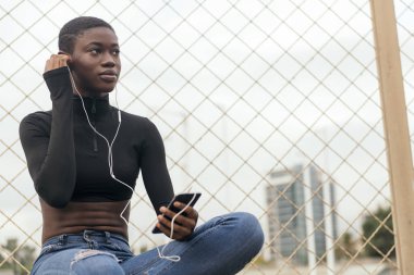 Kısa saçlı Afro-Amerikalı kadın kulaklık takıyor, cep telefonuyla müzik dinliyor, mesaj için yer kopyalıyor.