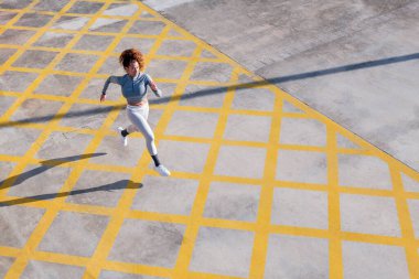 Spor giyimli kararlı kadın koşucunun güneş ışığındaki süs ve gölgelerle kaldırımda koşması, şehir sporu ve sağlıklı yaşam tarzı kavramı, metin için kopyalama alanı