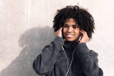 Kıvırcık saçlı afro-amerikan ergen çocuk mutlu bir şekilde gülümsüyor kulaklıkla müzik dinliyor, ergenlik kavramı ve genç yaşam tarzı, metin için kopya alanı